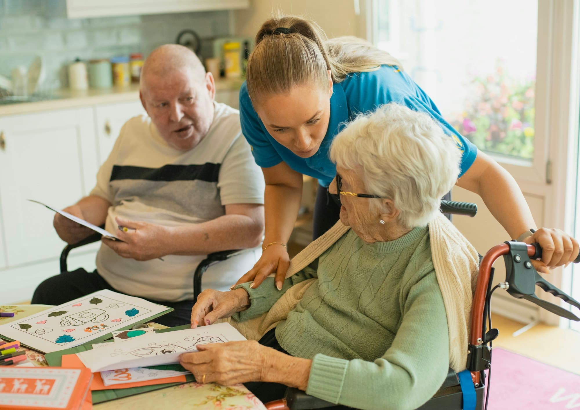 A friendly carer helping an older couple with a colouring activity at home